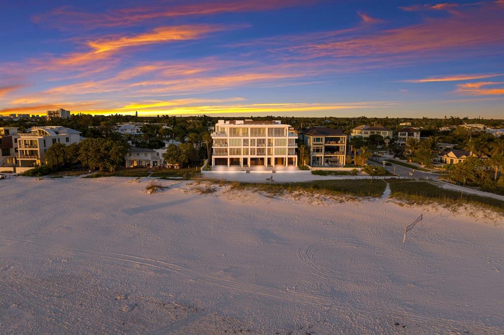 An aerial view of a modern multi-story beachfront building at sunset with a sandy beach — 84 AVENIDA VENECCIA UNIT 202 & 203, SARASOTA, FL