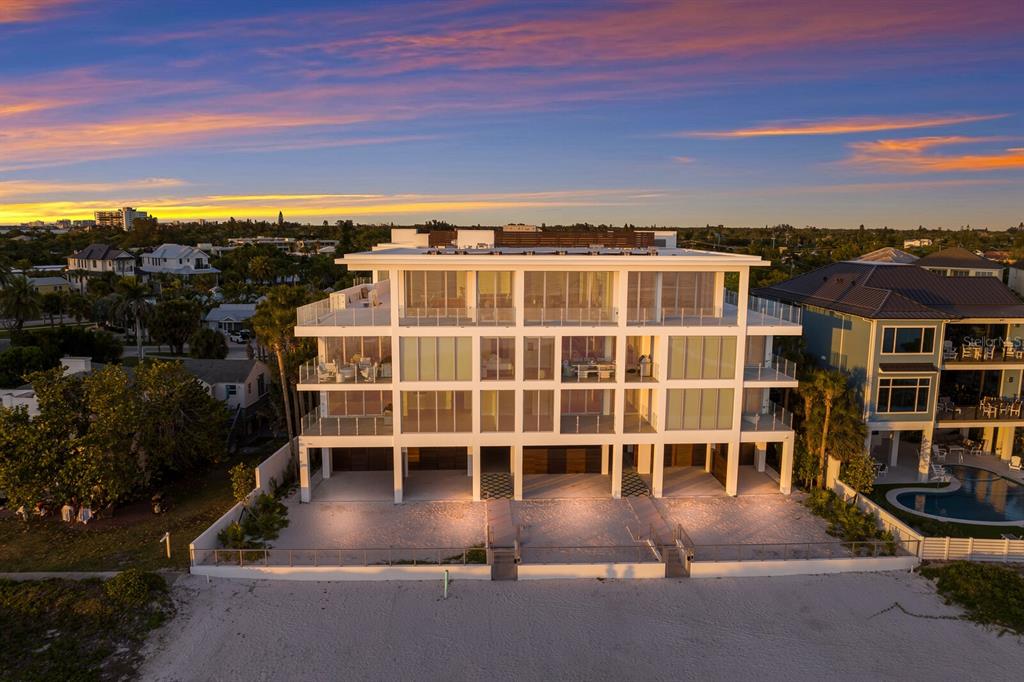 An aerial view of a modern, multi-story beachfront condominium building at sunset — 84 AVENIDA VENECCIA UNIT 202 & 203, SARASOTA, FL