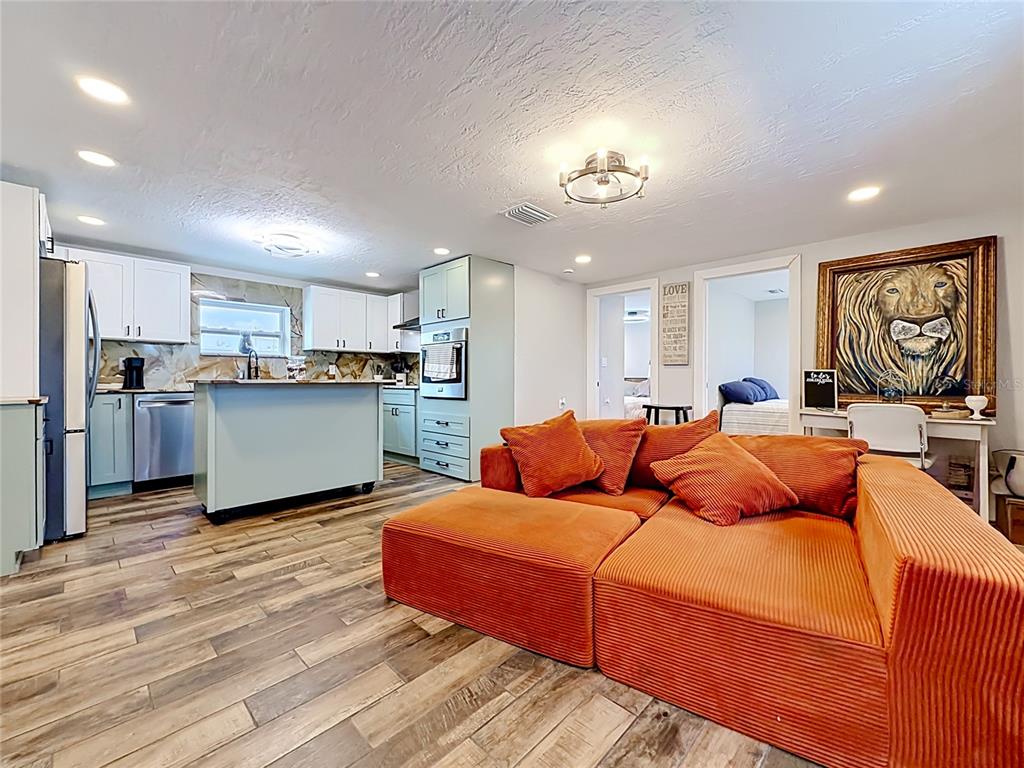 A living room with an orange sectional sofa faces an open kitchen with light-colored cabinetry — 1161 KEHOSEE LANE, ENGLEWOOD, FL