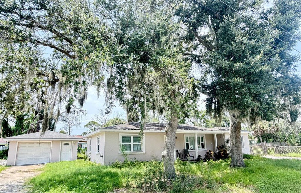 A single-story house with a detached garage sits under large, moss-draped oak trees — 8209 PAPAYA STREET, PORT RICHEY, FL
