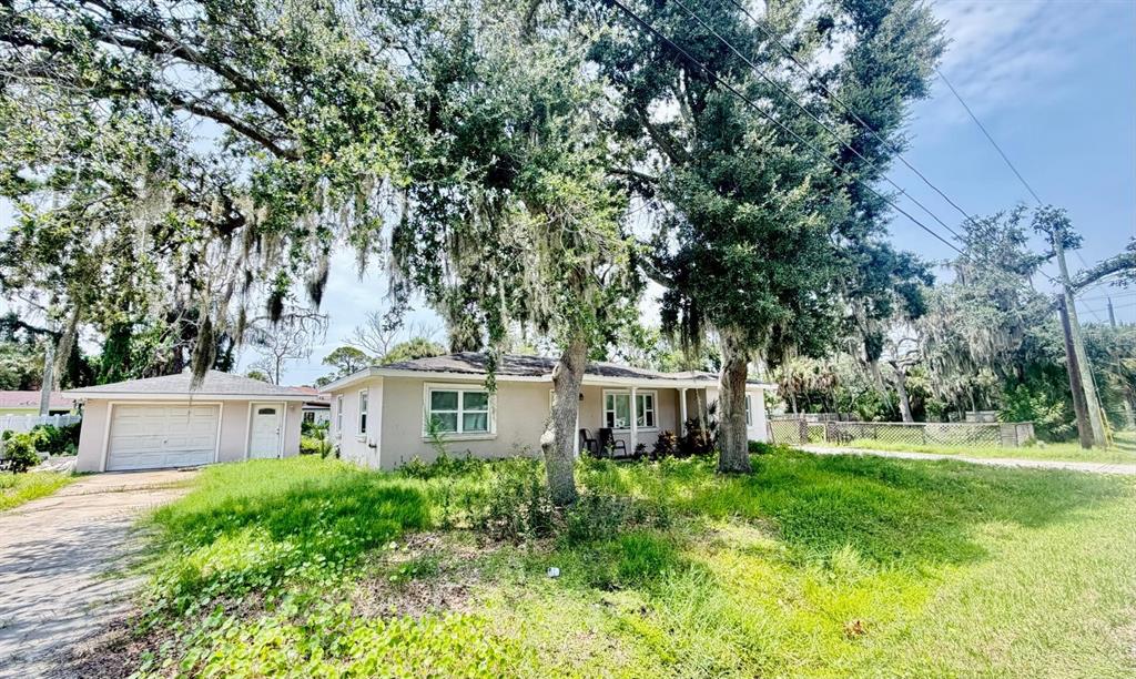 A single-story house with a detached garage sits on a grassy lot under large trees — 8209 PAPAYA STREET, PORT RICHEY, FL