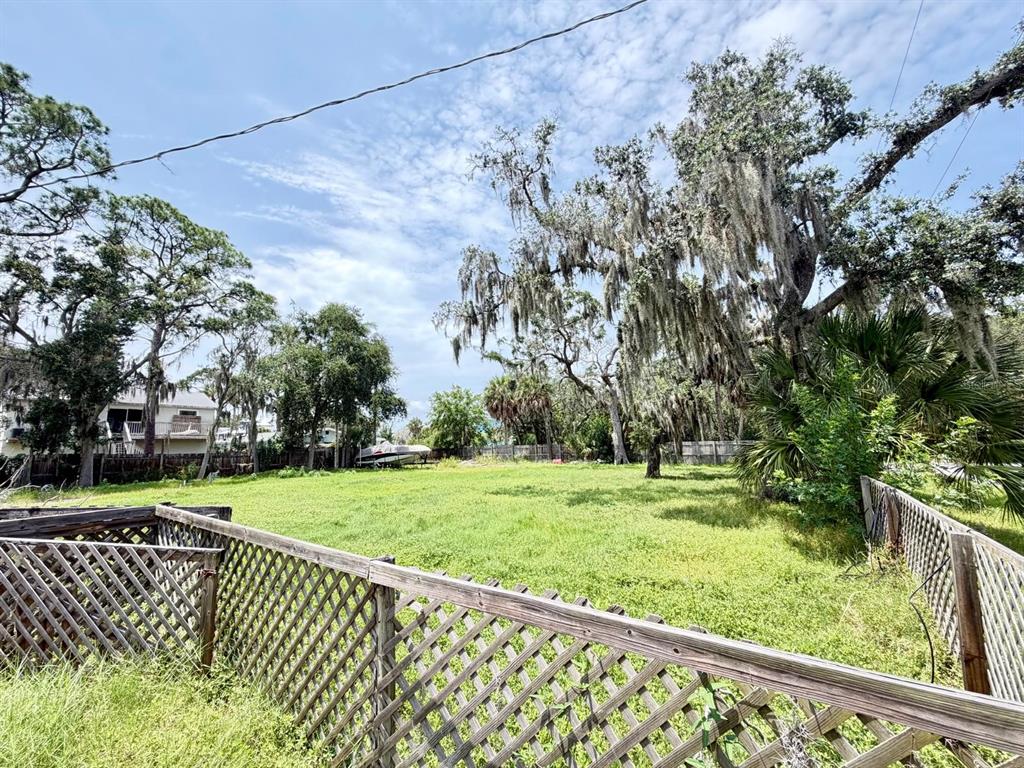 A grassy, fenced-in backyard features large oak trees draped with Spanish moss — 8209 PAPAYA STREET, PORT RICHEY, FL