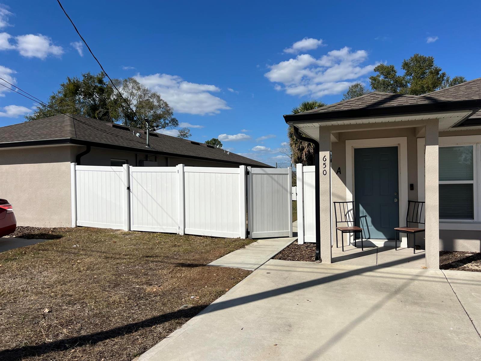 A white vinyl fence separates a concrete driveway from a house with a blue door — 650 E Grapefruit Avenue # A, FL 33850, FL