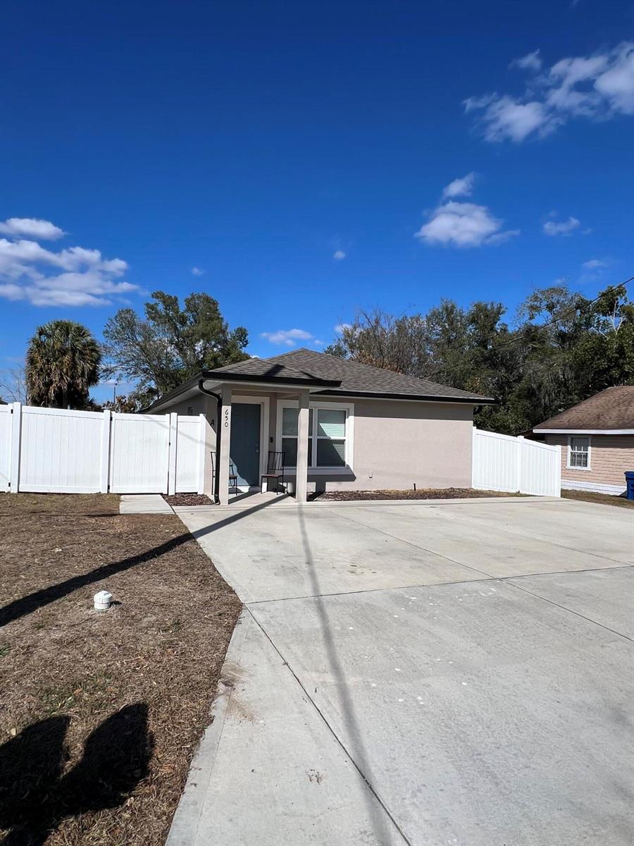 A single-story tan house with a concrete driveway and white vinyl fencing under a blue sky — 650 E Grapefruit Avenue # A, FL 33850, FL
