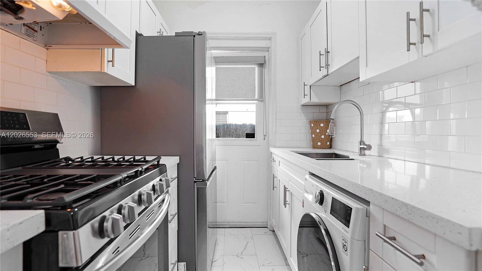 A galley kitchen features white cabinets, a stainless steel refrigerator, a gas stove, and laundry — 815 W 39, Miami Beach FL 33140, MIAMI BEACH, FL