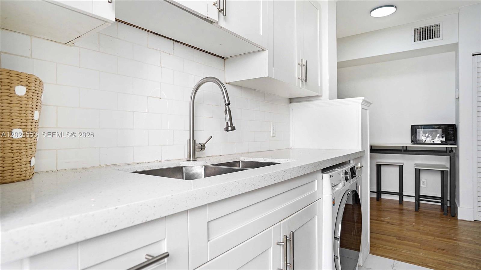 A white kitchen features a stainless steel sink, subway tile backsplash, and an integrated washer — 815 W 39, Miami Beach FL 33140, MIAMI BEACH, FL