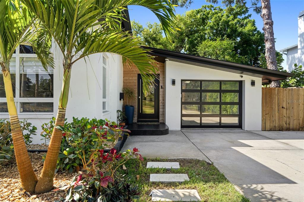 A modern home exterior features a glass garage door, wood-paneled entryway, and a palm tree — 6228 7TH AVENUE N, ST PETERSBURG, FL