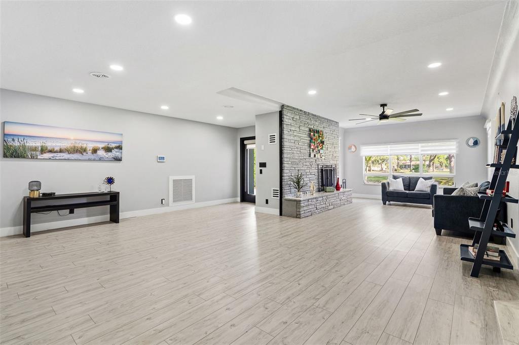 A spacious living room features light wood-look flooring, a stone fireplace, and recessed lighting — 6228 7TH AVENUE N, ST PETERSBURG, FL