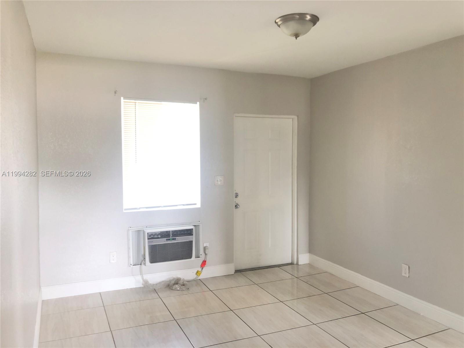 A room with light-colored tile flooring, a window air conditioner, and a white door — 1940 Washington Ave # 11, Opa-Locka FL 33054, OPA-LOCKA, FL