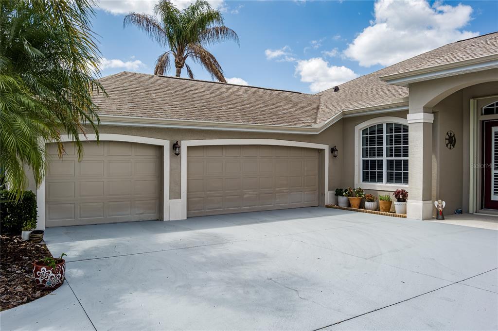 The exterior of a house features a three-car garage, a concrete driveway, and a palm tree — 11220 28TH STREET CIRCLE E, PARRISH, FL
