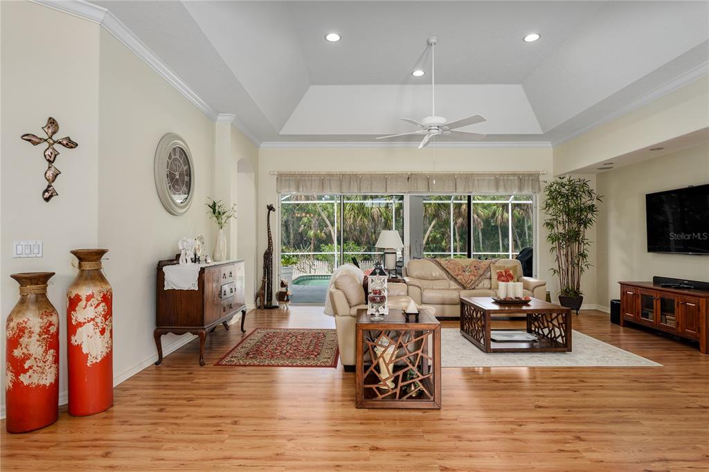 A living room features wood-look flooring, a tray ceiling, and a view of a pool — 11220 28TH STREET CIRCLE E, PARRISH, FL