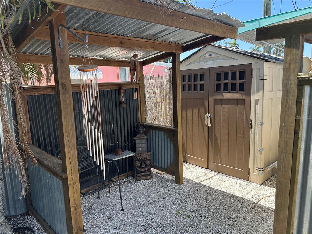 A covered outdoor seating area with a wind chime sits beside a tan storage shed — 3723 116TH STREET W, BRADENTON, FL
