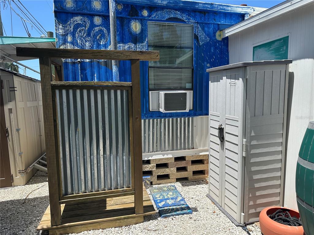 An outdoor shower with a corrugated metal screen stands beside a blue mural-painted mobile home — 3723 116TH STREET W, BRADENTON, FL
