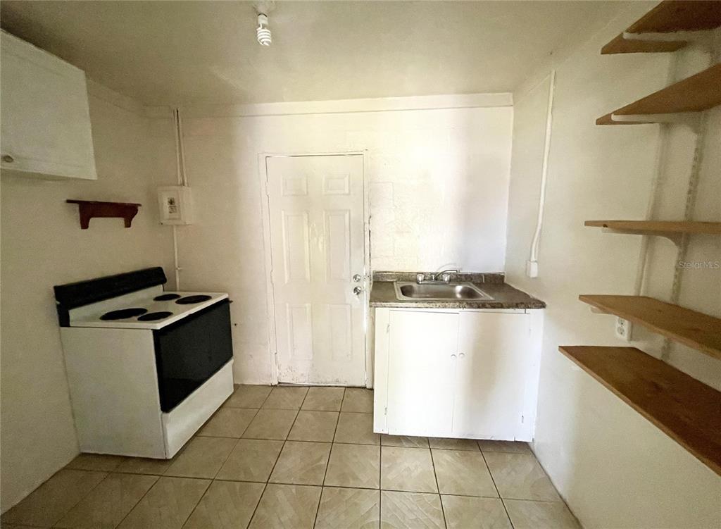 A small kitchen features a white stove, a single sink cabinet, and open wall shelving — 131 B STREET UNIT 3, LAKE WALES, FL