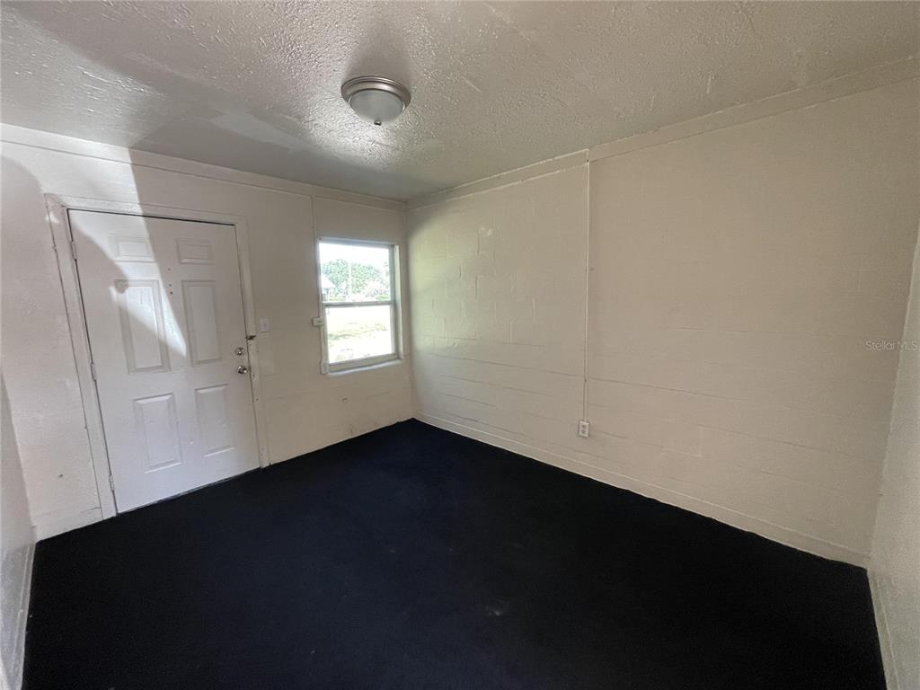 An empty room features white painted block walls, a dark carpet, and a single door — 131 B STREET UNIT 3, LAKE WALES, FL