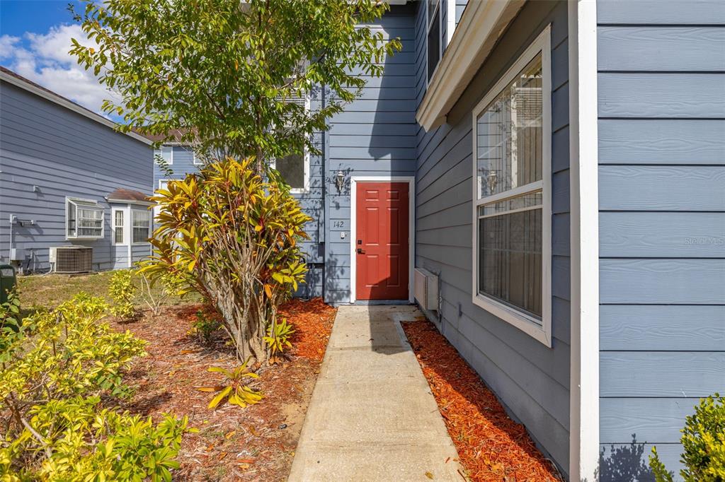 A concrete walkway leads to a red front door on a blue-sided residential building — 142 MANGO DRIVE, DAVENPORT, FL