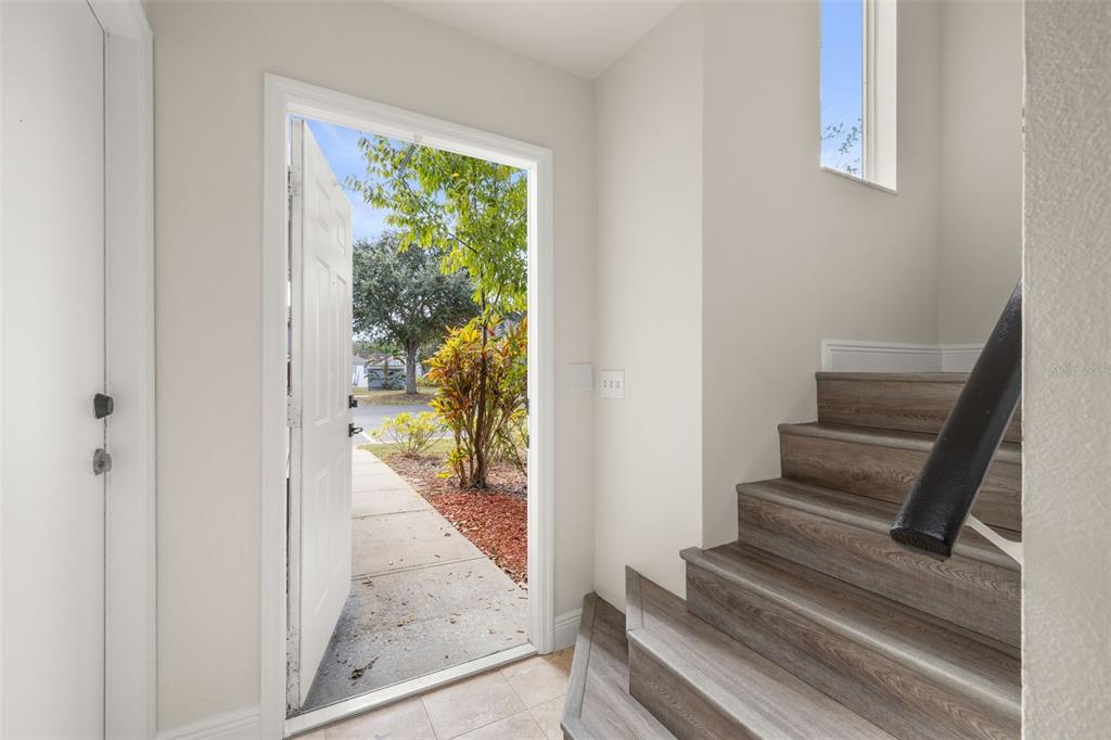 An open front door reveals a view of a yard next to a wooden staircase — 142 MANGO DRIVE, DAVENPORT, FL