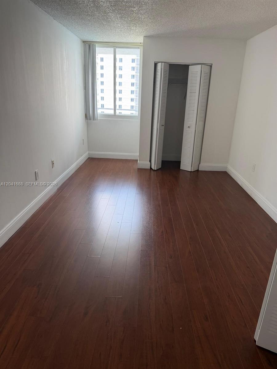 An empty bedroom features dark wood-look flooring, white walls, and a white bi-fold closet door — 800 N Miami Ave # E1402, Miami FL 33136, MIAMI, FL