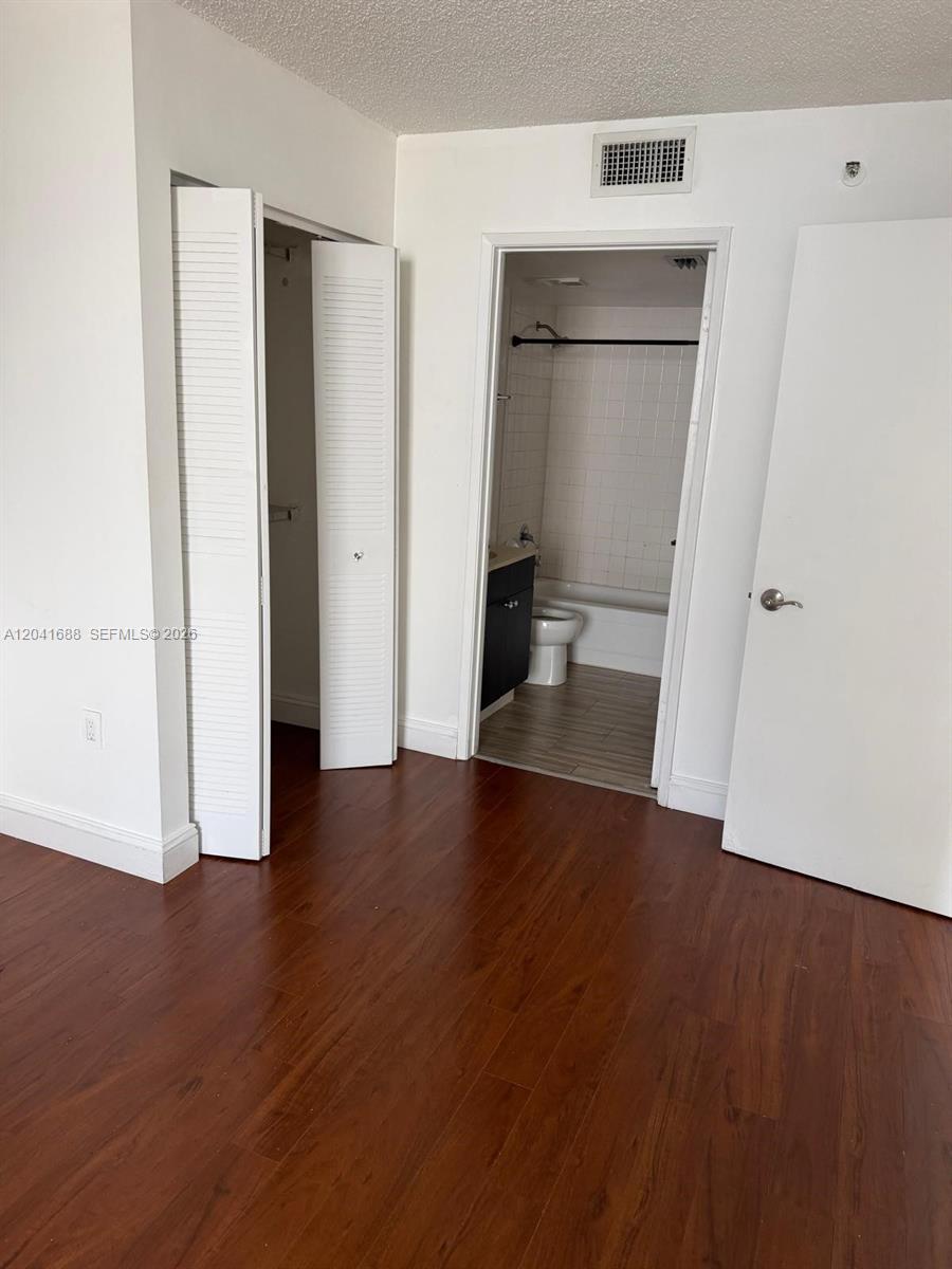 A room with wood-look flooring features a closet with louvered doors and an adjacent bathroom — 800 N Miami Ave # E1402, Miami FL 33136, MIAMI, FL