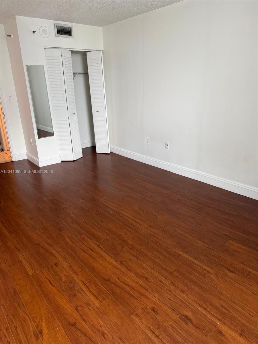 An empty room features dark wood-look flooring, white walls, and a white bi-fold closet door — 800 N Miami Ave # E1402, Miami FL 33136, MIAMI, FL