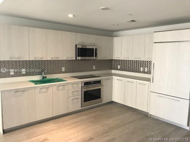 A modern kitchen features light wood cabinets, stainless steel appliances, and a tiled backsplash — 55 SW 9th St # 2510, Miami FL 33130, MIAMI, FL