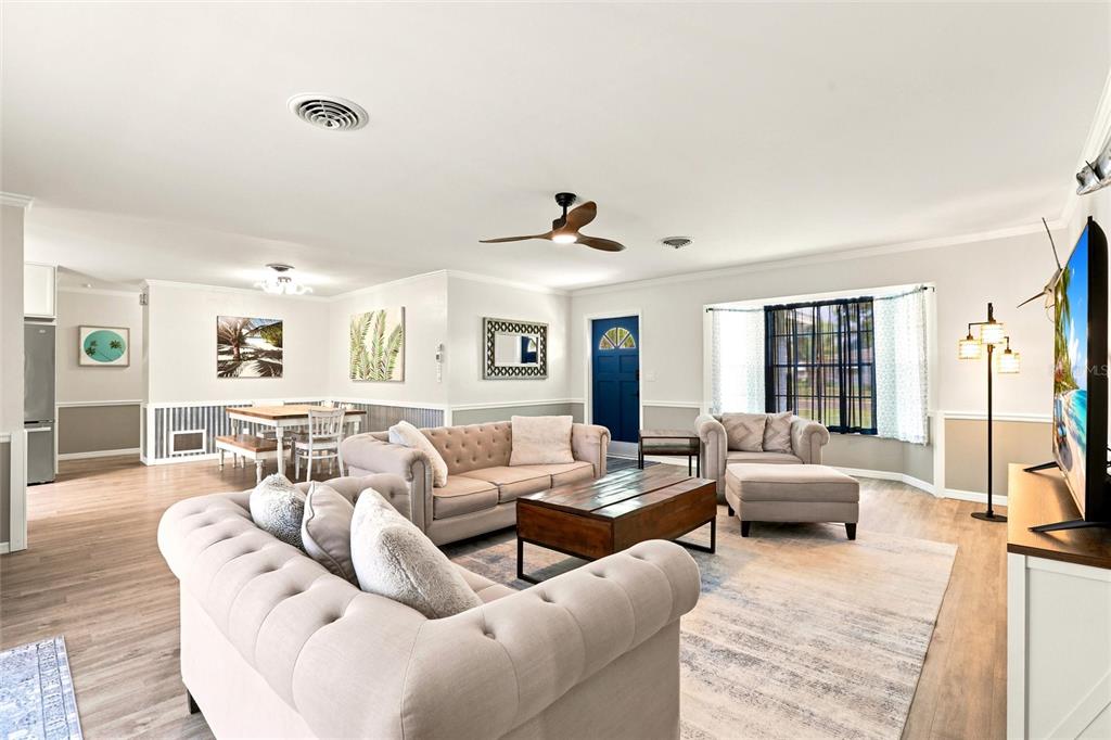 A living room with light wood floors, tufted sofas, a coffee table, and dining area — 1795 ELINOR PLACE, ENGLEWOOD, FL