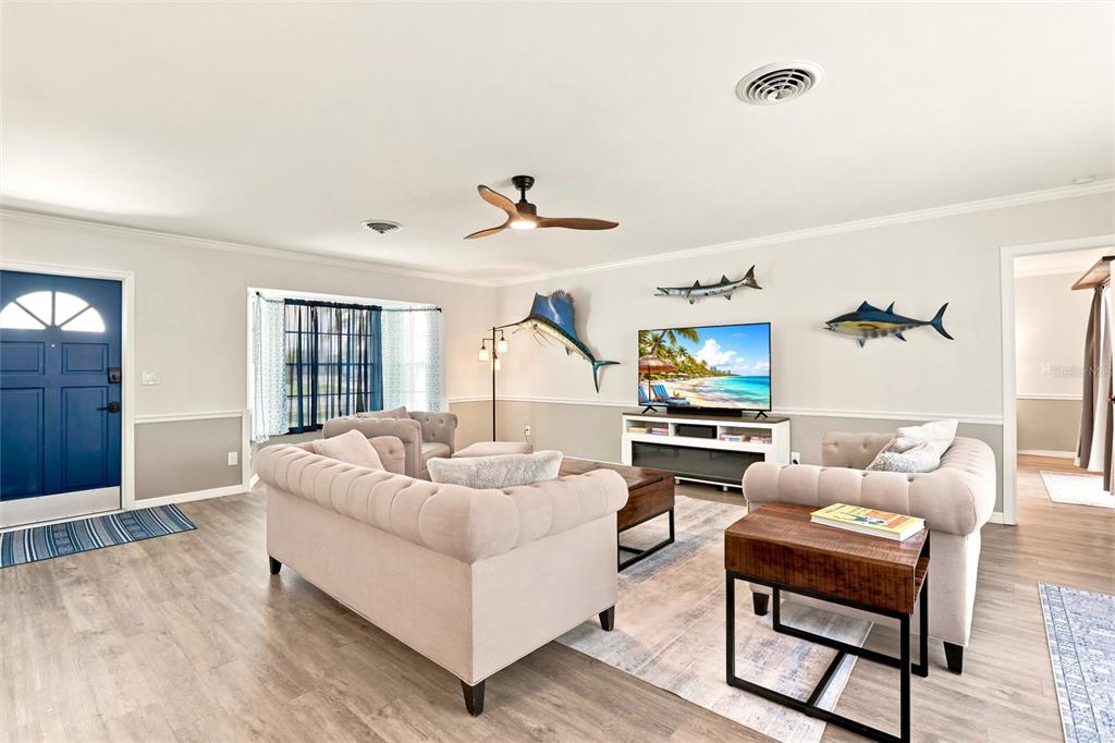 A living room features light wood flooring, two tufted sofas, and mounted fish wall decor — 1795 ELINOR PLACE, ENGLEWOOD, FL