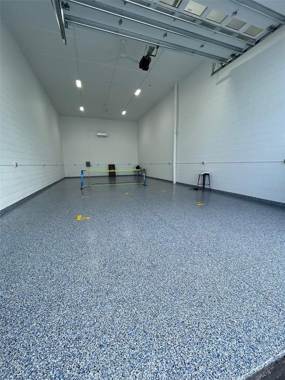 An empty garage features a speckled epoxy floor, white block walls, and a pickleball net — 5233 TAYLOR ROAD UNIT B1, PUNTA GORDA, FL