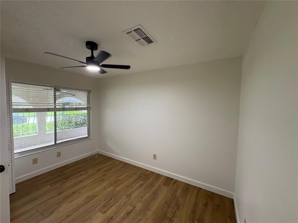 An empty room features light-colored walls, wood-look flooring, a ceiling fan, and a large window — 4824 GALLANT LANE, ORLANDO, FL