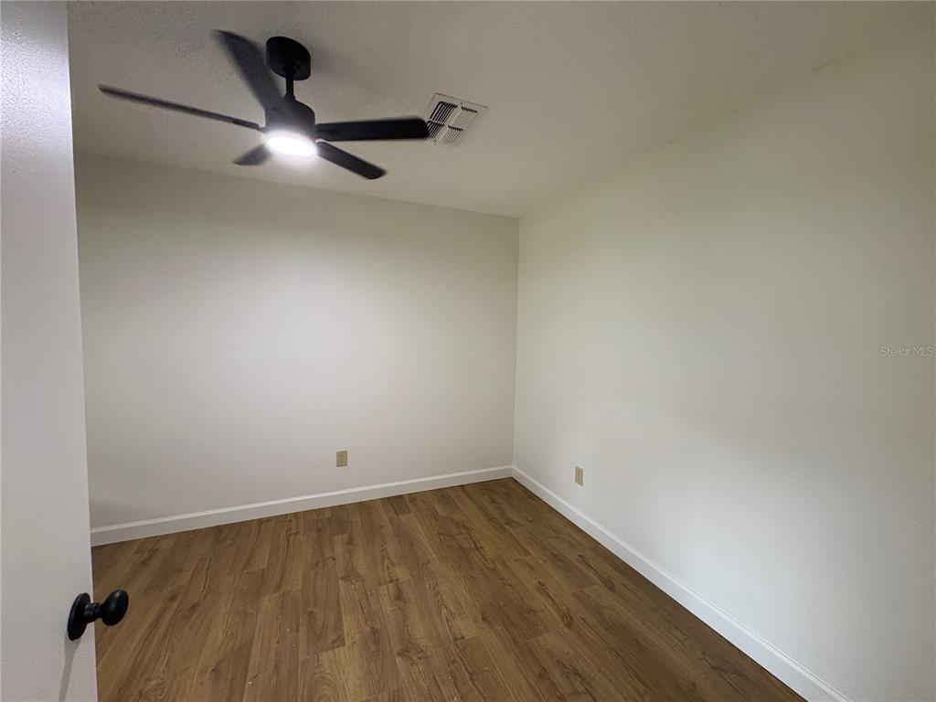 An empty room features wood-look flooring, white walls, and a black ceiling fan — 4824 GALLANT LANE, ORLANDO, FL