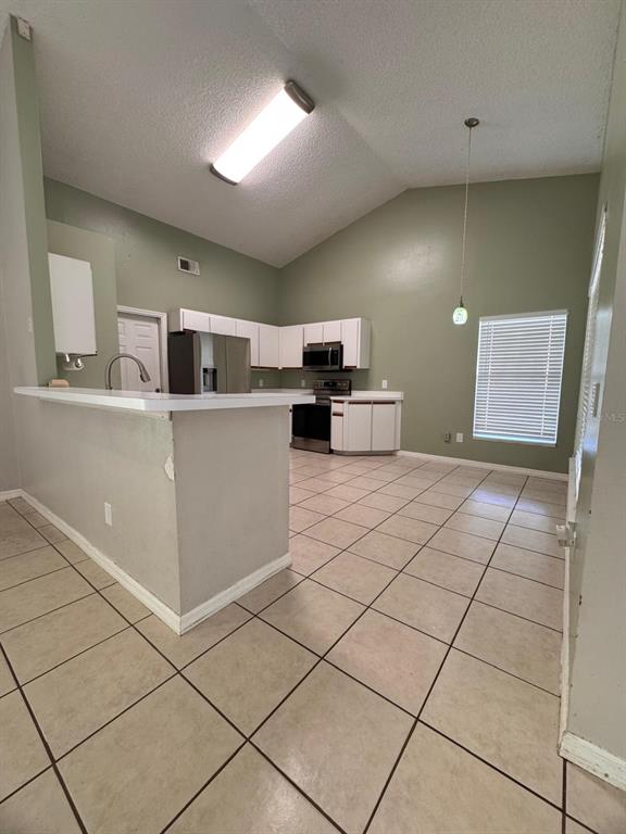 A kitchen with white cabinets, stainless steel appliances, and tile flooring under a vaulted ceiling — 40045 PALM STREET, LADY LAKE, FL