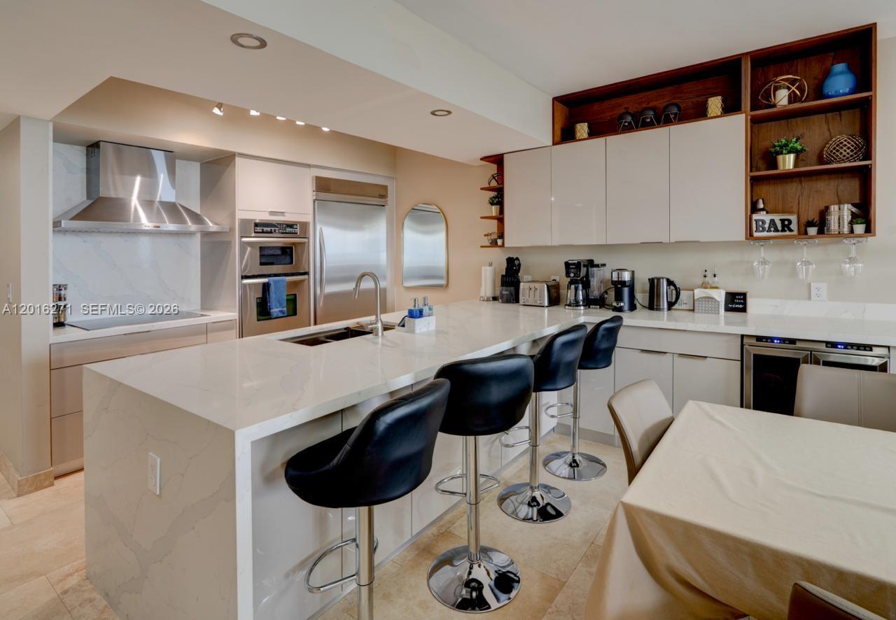 A modern kitchen features a white quartz island, black bar stools, and stainless steel appliances — 1830 S Ocean Dr # 4903, Hallandale Beach FL 33009, HALLANDALE BEACH, FL