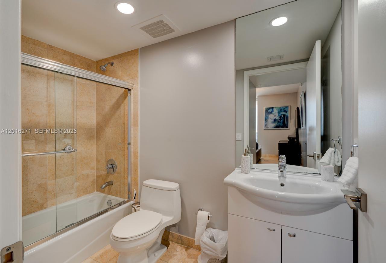 A bathroom features a glass-enclosed shower-tub combo, a white vanity, and tan tile flooring — 1830 S Ocean Dr # 4903, Hallandale Beach FL 33009, HALLANDALE BEACH, FL