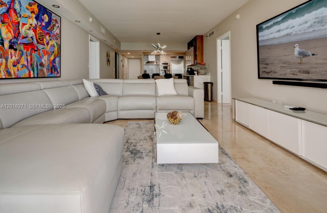 A modern living room features a white sectional sofa, glass coffee table, and large television — 1830 S Ocean Dr # 4903, Hallandale Beach FL 33009, HALLANDALE BEACH, FL