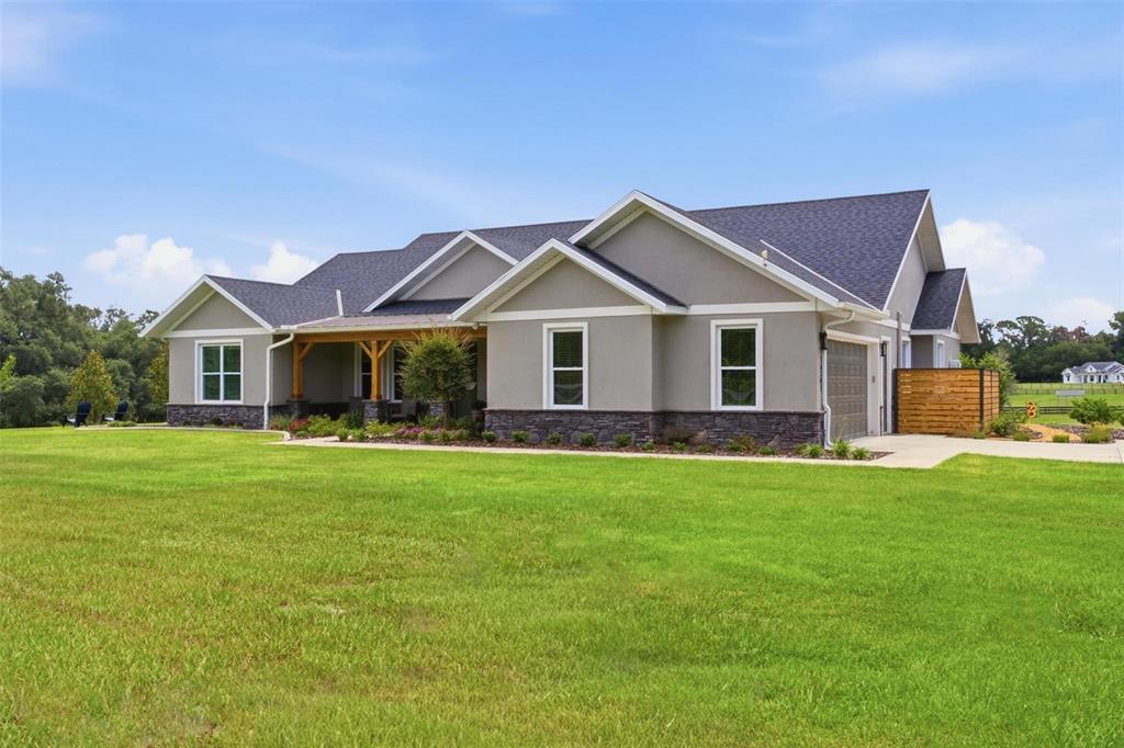 A rectangular swimming pool sits on a stone patio behind a house with a porch — 16241 SE 150TH AVENUE, WEIRSDALE, FL