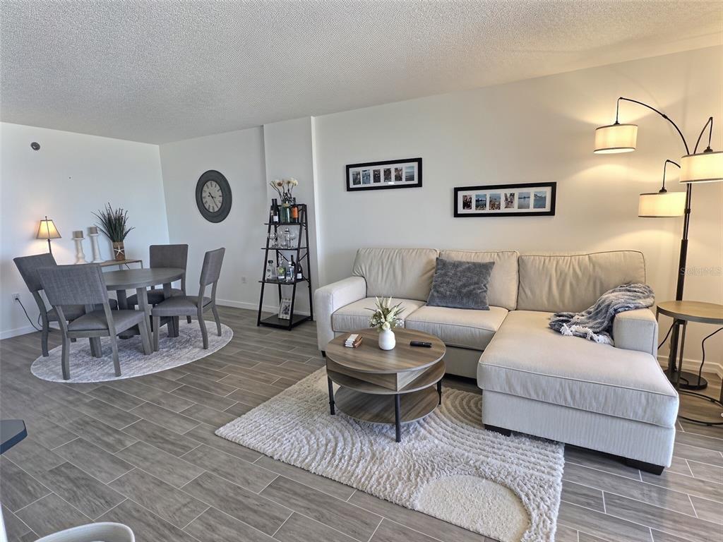 A living and dining area features a sectional sofa, round table, and wood-look tile flooring — 3006 CARING WAY UNIT 602, PORT CHARLOTTE, FL