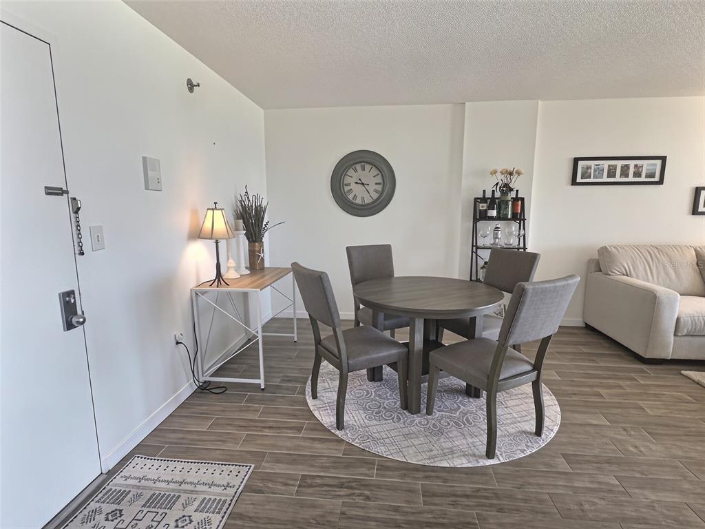 A dining area features a round wooden table, four gray chairs, and a wall clock — 3006 CARING WAY UNIT 602, PORT CHARLOTTE, FL