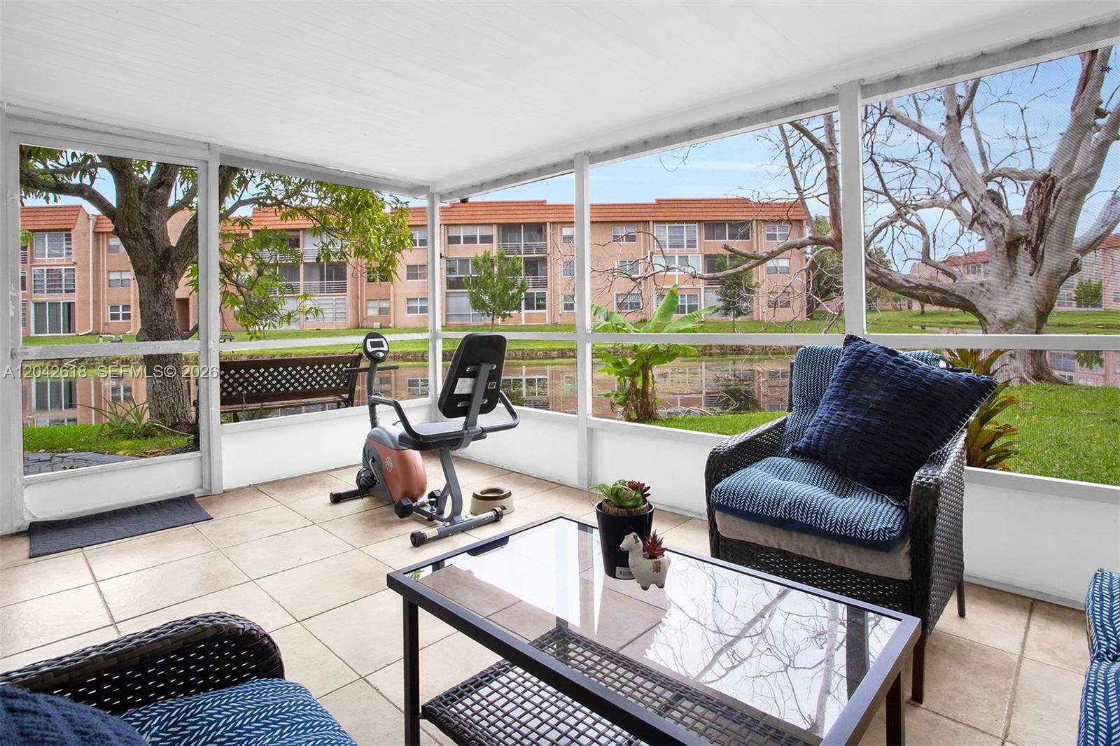 A screened-in patio features tile flooring, a stationary bike, and outdoor furniture overlooking a pond — 9675 NW 26th Pl # 5, Sunrise FL 33322, SUNRISE, FL