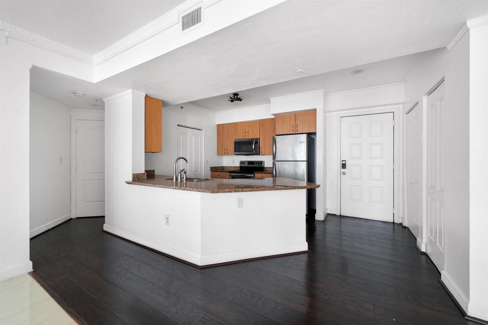 A kitchen with wood cabinets, granite countertops, and dark hardwood floors opens to a living area — 1830 Radius Drive # 405, Hollywood FL 33020, HOLLYWOOD, FL