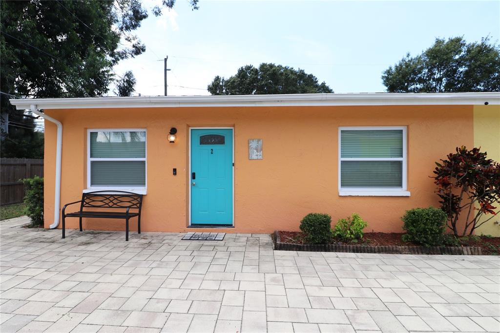 An orange exterior wall features a turquoise front door, two windows, and a metal bench — 1635 GLADYS STREET UNIT 2, LARGO, FL