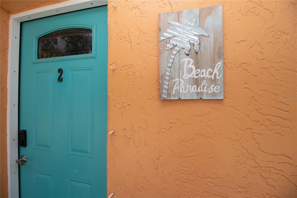 A teal door with the number two sits next to a wooden beach paradise sign — 1635 GLADYS STREET UNIT 2, LARGO, FL