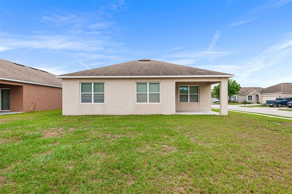 The exterior rear view of a single-story beige house with a covered patio and lawn — 4140 SOPHIA BOULEVARD, WINTER HAVEN, FL