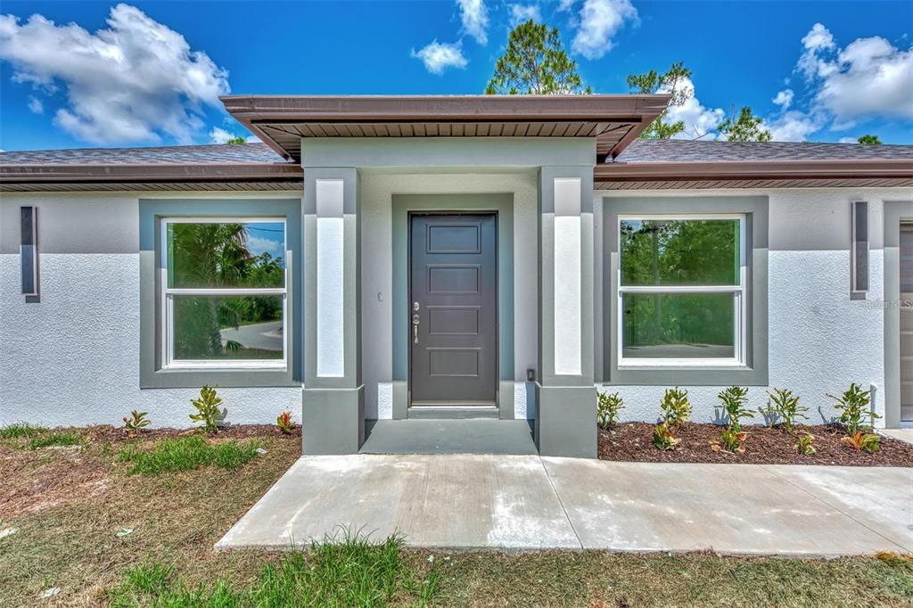 A front exterior view of a house featuring a dark door and two large windows — 5465 TYSON STREET, NORTH PORT, FL