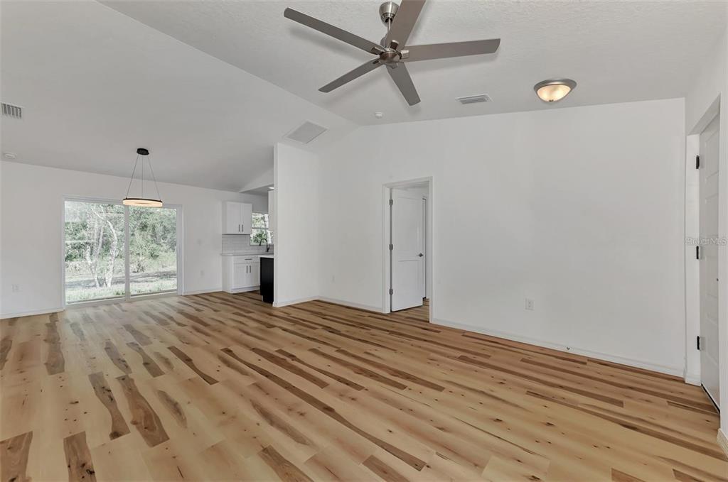 A bright, open-concept living area features light wood flooring, a ceiling fan, and sliding doors — 5465 TYSON STREET, NORTH PORT, FL