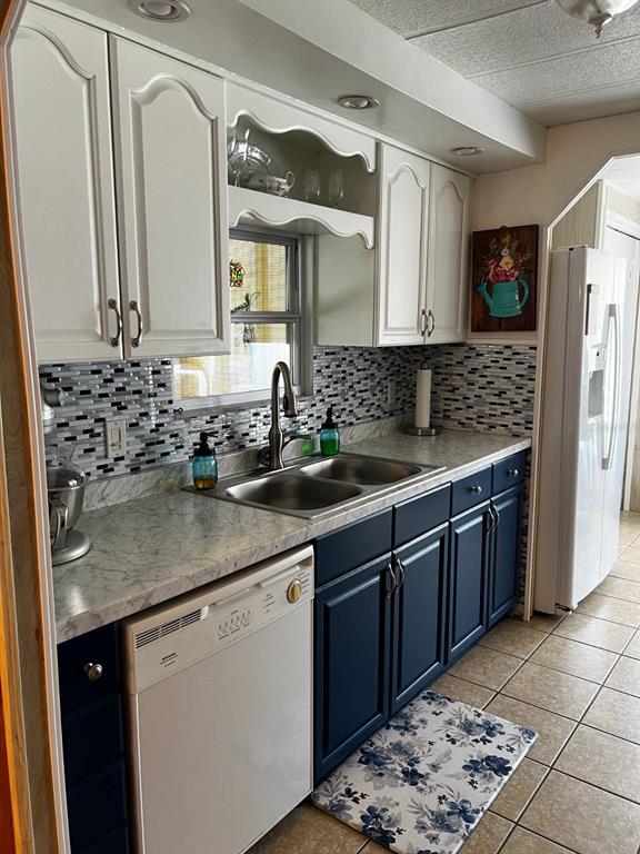 A kitchen features white upper cabinets, dark blue lower cabinets, and a mosaic tile backsplash — 15 WILDERNESS DRIVE, LAKE PANASOFFKEE, FL