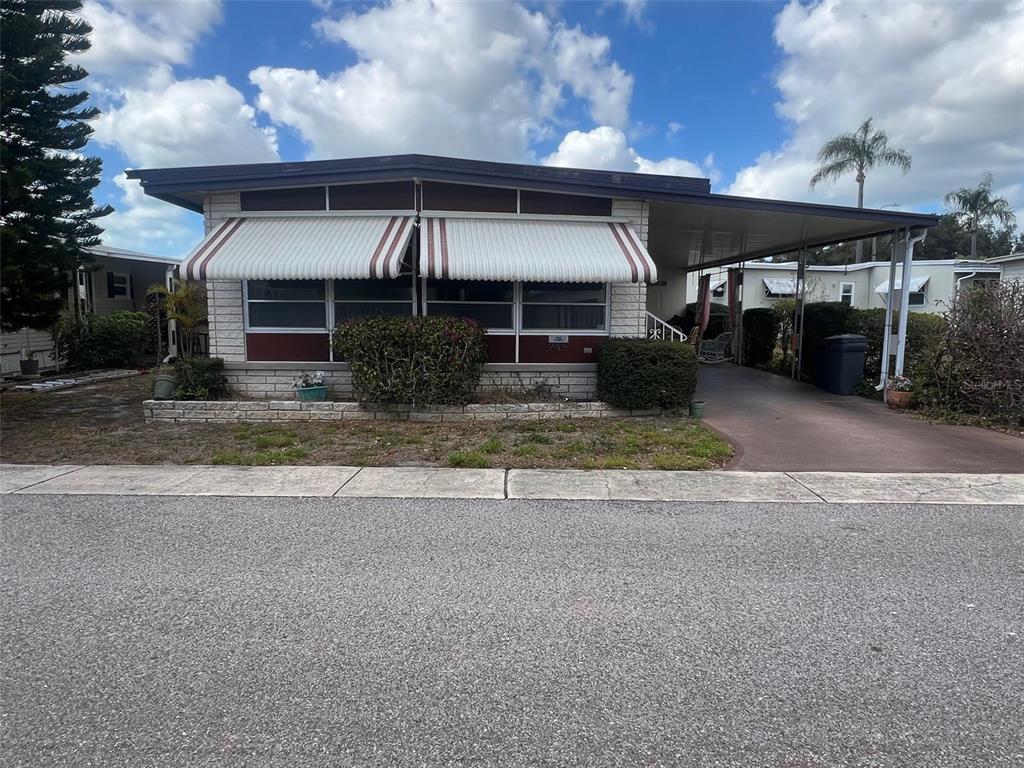 A single-story manufactured home with a carport, metal awnings, and a brick-patterned foundation — 29250 US HIGHWAY 19 N UNIT 248, CLEARWATER, FL