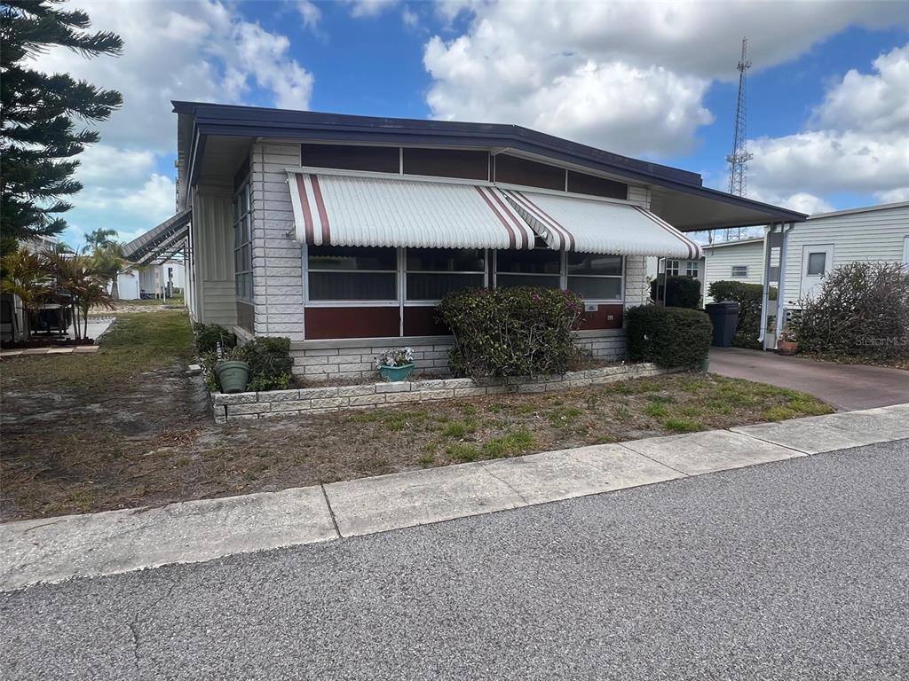 A single-story mobile home features a white brick facade, striped awnings, and a carport — 29250 US HIGHWAY 19 N UNIT 248, CLEARWATER, FL