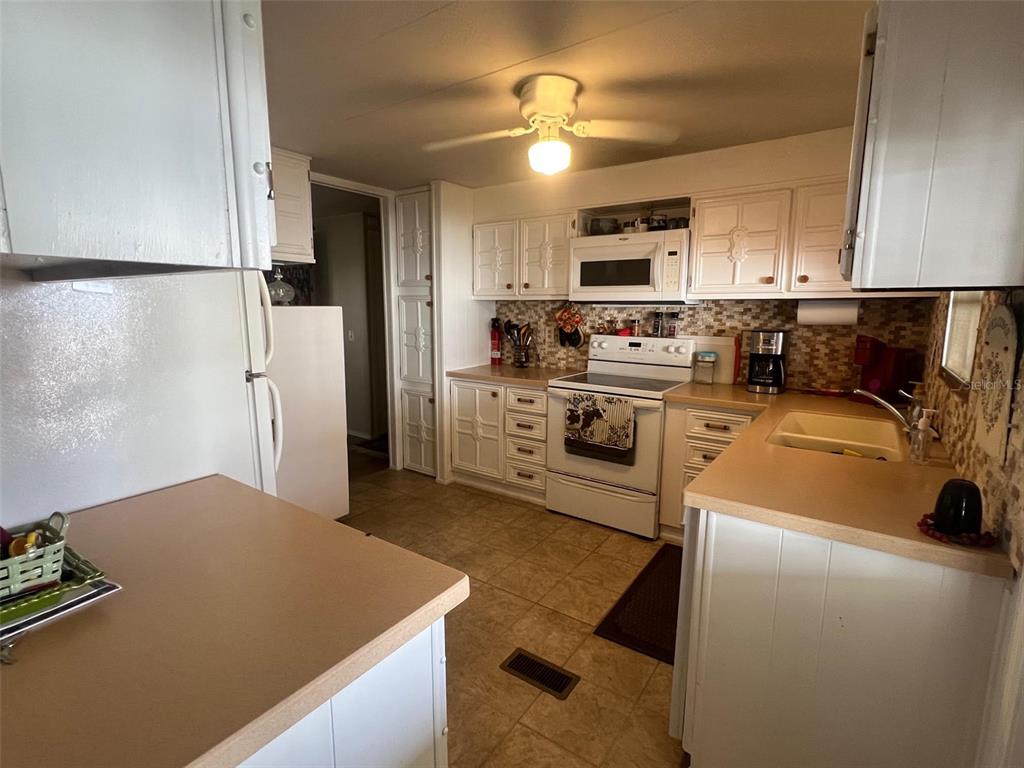 A kitchen features white cabinetry, a light-colored countertop, a white stove, and a ceiling fan — 29250 US HIGHWAY 19 N UNIT 248, CLEARWATER, FL
