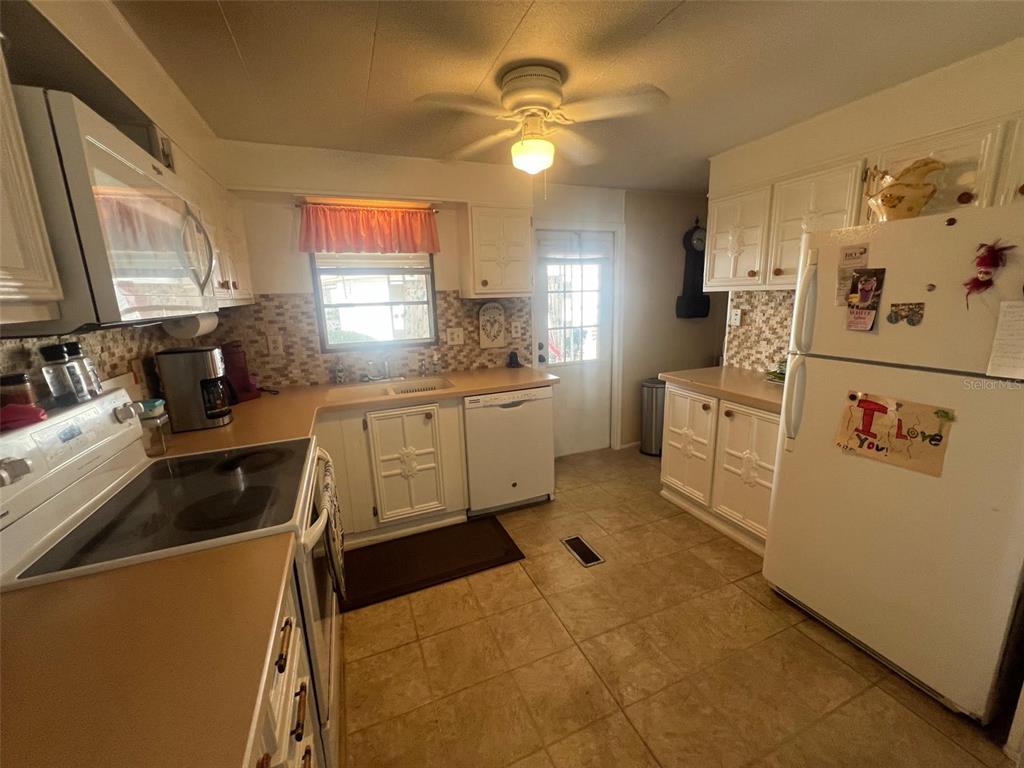A kitchen features white cabinets, tan countertops, a tiled backsplash, and a white refrigerator — 29250 US HIGHWAY 19 N UNIT 248, CLEARWATER, FL