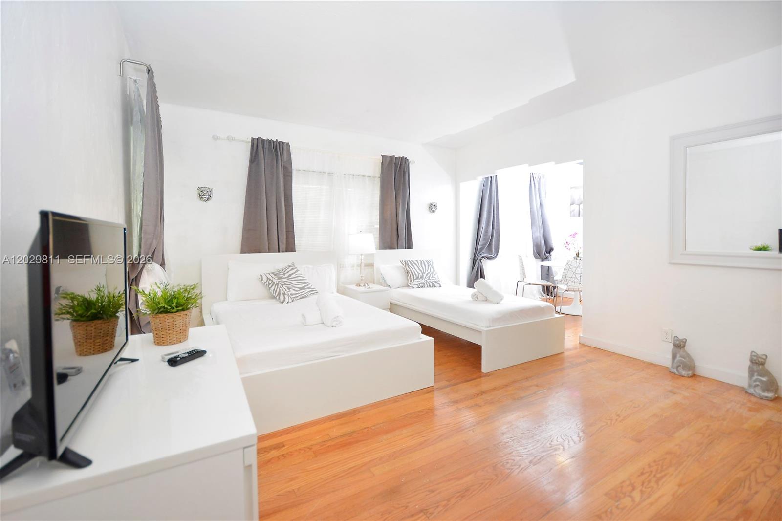 A bedroom features two white beds, hardwood floors, and a television on a white stand — 1021 Euclid Ave # 1, Miami Beach FL 33139, MIAMI BEACH, FL